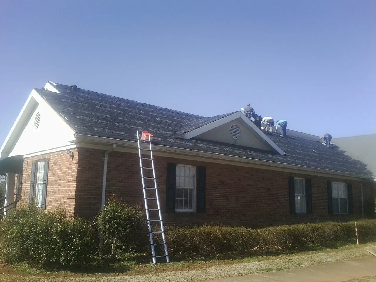 Crew tearing shingles off a brick ranch roof with a ladder set — Emergency Roof Repair work by our crew in Newfield