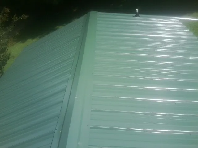 New green metal panels meeting at the ridge of a roof — Flat Roof Repair work by our crew in Newfield